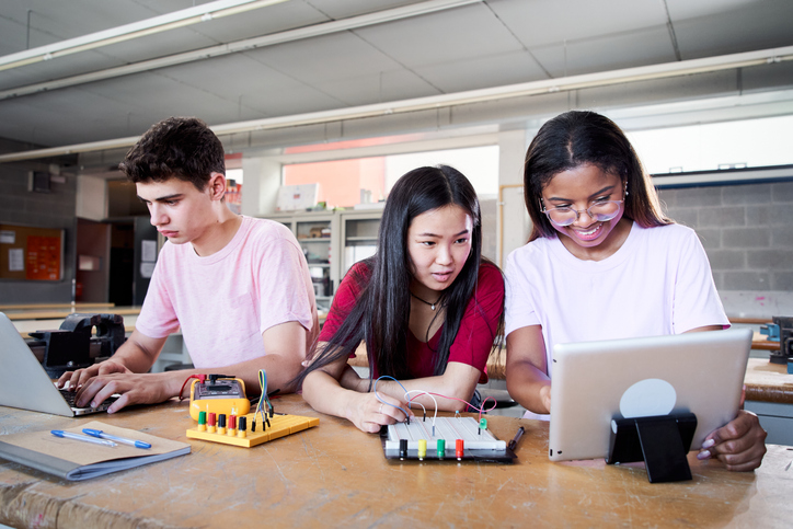 Three middle-school aged students working on a technical project with their laptops.